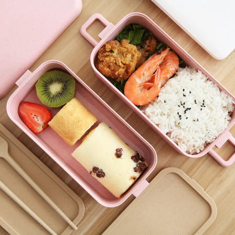 Pink bento box with compartments containing food on a wooden surface